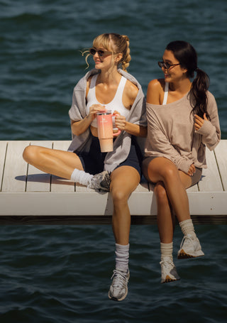 Two Women Sitting On Dock With One Holding The Stanley Summer Quencher Tumbler