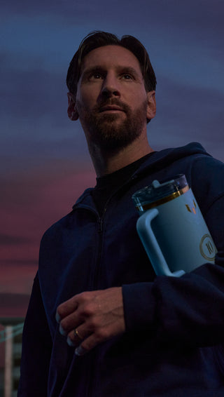 Lionel Messi standing at sunset holding a Stanley x Messi limited edition bottle in Messi Blue with gold accents and number 10 detailing