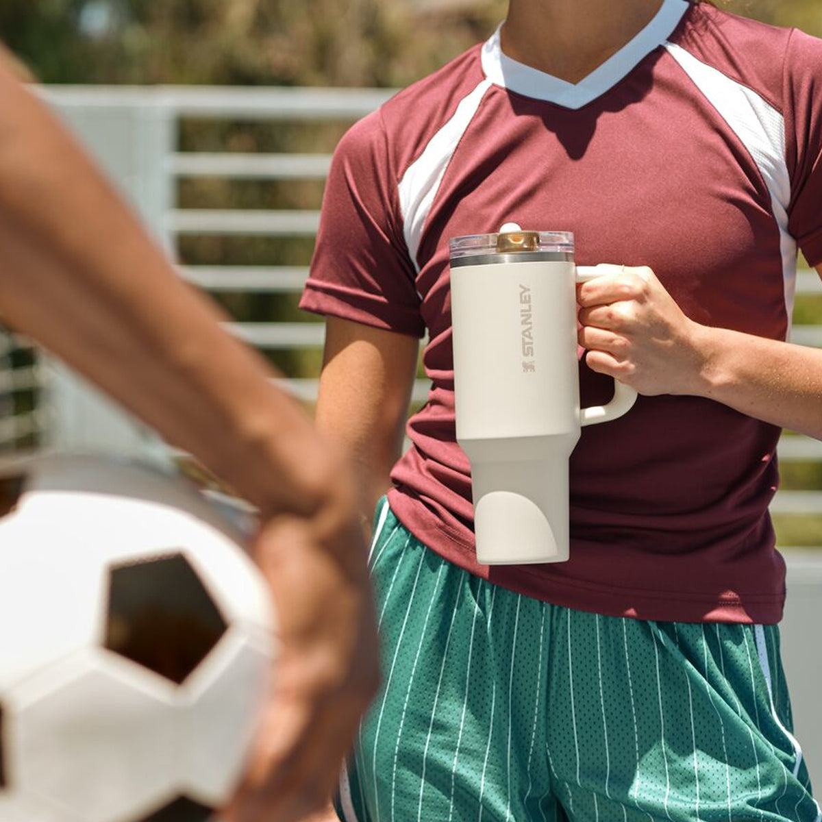 Stanley 1913 cream tumbler with handle held by soccer player in maroon jersey, soccer ball in foreground