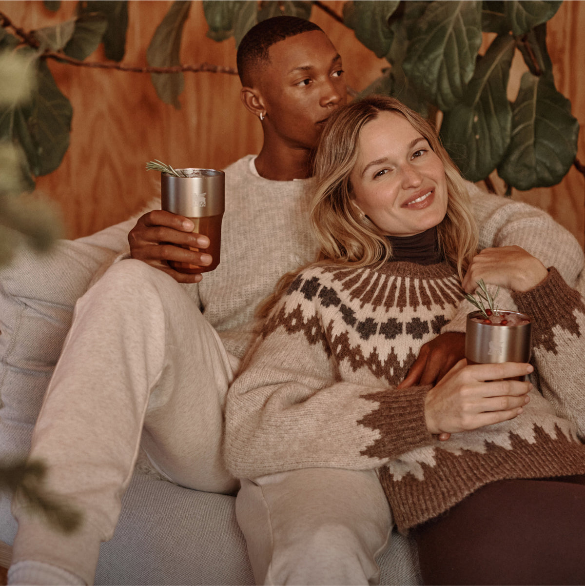 Two people relaxing together holding Stanley 1913 stainless steel tumblers with rosemary garnishes in a cozy autumn setting.